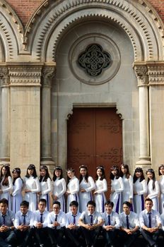 HO CHI MINH CITY, VIET NAM- NOV 24: Crowd of Vietnamese student in traditional dress, ao dai, shooting for yearbook at Saigon Notre Dame Cathedral, Vietnam, Nov 24, 2015