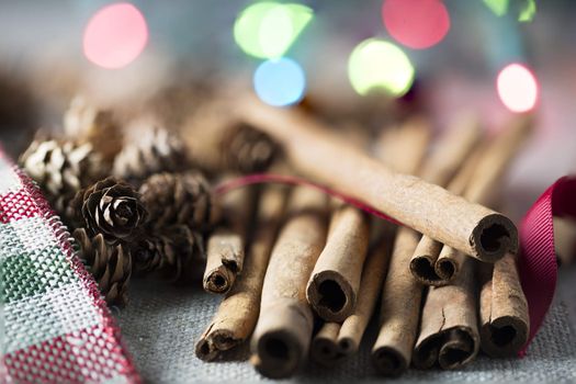Cinnamon sticks close up with small pine cones and festive holiday lights in the background