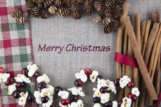 Linen fabric printed with Merry Christmas surrounded by cinnamon sticks, popcorn garland and pine cones.