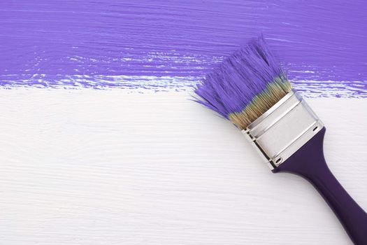 Horizontal stripe of purple paint with a dirty paintbrush on a white wooden board