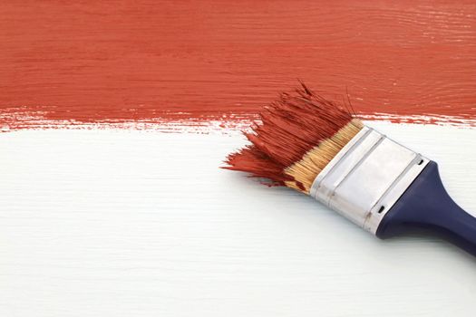 Paintbrush loaded with red paint, painting over white wooden board