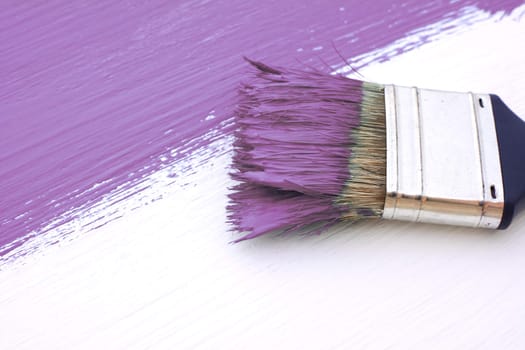 Close-up of paintbrush with paint-covered bristles painting a white board purple