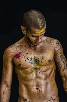 Attractive young man shirtless, skin painted all over with bright Honi colors, looking down