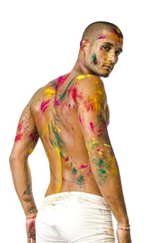 Attractive young man shirtless, turning around, with skin painted all over with bright Holi colors, looking at camera, isolated on white background