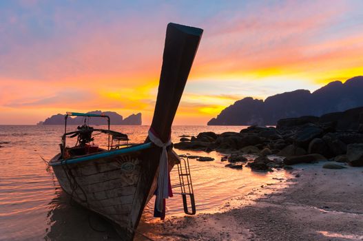 Traditional thai wooden longtail boat on beach of Phi-Phi Don island in sunset. Silhouette of famous Phi Phi Lee island in background. Thailand, Krabi province.