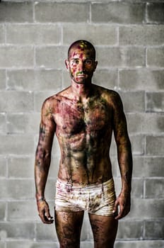 Handsome young man with skin painted all over with bright Holi colors, in front of concrete bricks wall