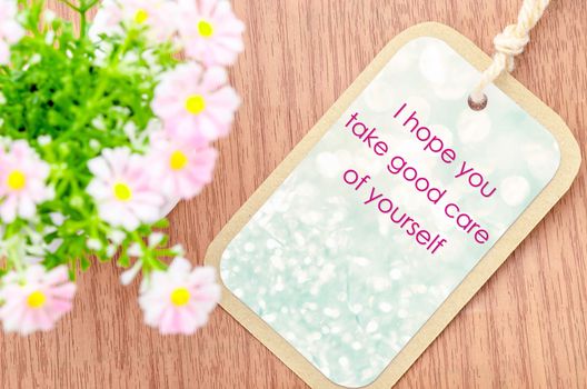 Take care of yourself greeting card with pink flower on wooden background.