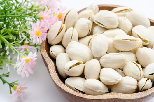 Pistachios nuts in a wooden bowl with pink flower.