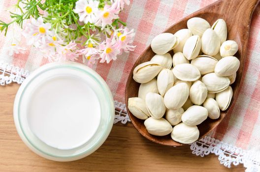 Raw Organic Pistachio Nuts and milk with pink flower on wooden background.