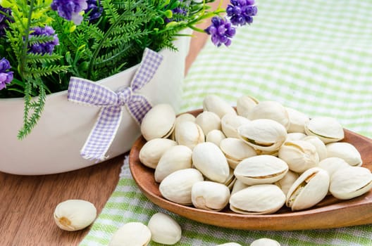 Roasted pistachios in wooden spoon with flower on wooden background.