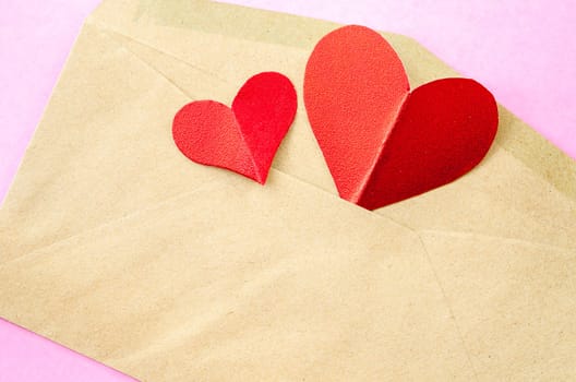 red heart paper in brown envelopes on pink background.
