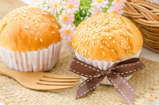 Bread bun with white sesame seeds and wooden spoon on white background