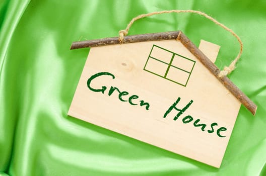 Green house concept. Wooden house shape on green fabric background.