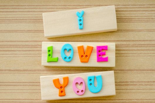 Inscription I LOVE YOU made of colorful letters on wooden background