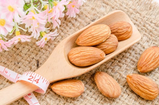 Almonds in wooden spoon with measure tape on sack background. Diet concept.