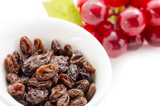 Dried raisins in white cup and fresh red grapes on a white background