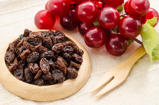 Raisins on a wooden dish and fresh red grapes on fabric background.