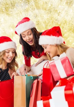 sale, winter holidays, christmas and people concept - smiling young woman in santa helper hat with gifts and shopping bags over yellow lights background