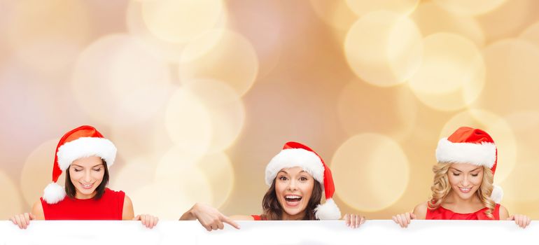 christmas, x-mas, people, advertisement and sale concept - happy women in santa helper hat with blank white board over beige lights background