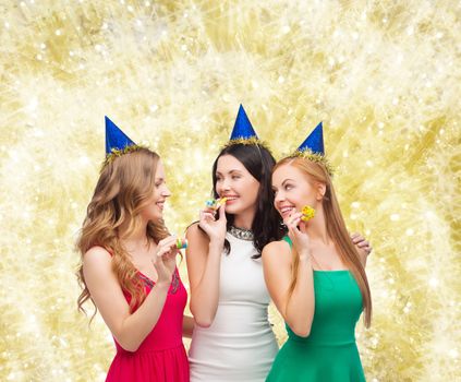 holidays, people and celebration concept - smiling women in party caps blowing to whistles over yellow lights background