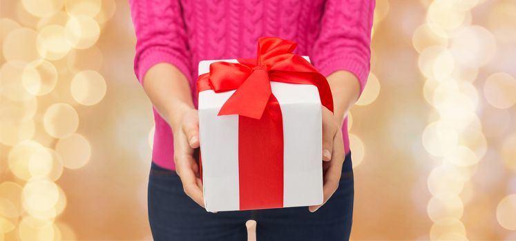 christmas, holidays and people concept - close up of woman in pink sweater holding gift box over beige lights background