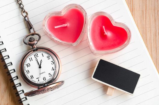 Red heart candle and pocket watch with open diary on wooden background.