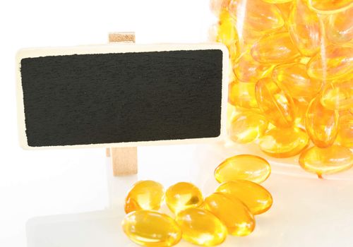Fish oil capsules on white background and blank wooden tag.
