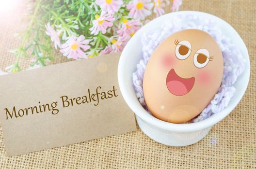 Morning breakfast and smile face egg in white cup with flower on sack background.