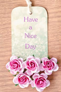 Have a nice day on beautiful tag pink rose on wooden background.