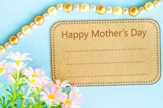 Happy mother's day on brown paper tag and pink flower on blue background for your text.