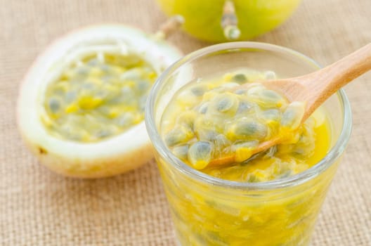 Passion fruit juice in glass with wooden spoon on sack background.