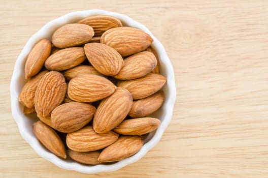 Almonds in white cup on wooden background.