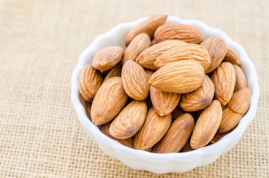 Almonds in white cup on sack background.