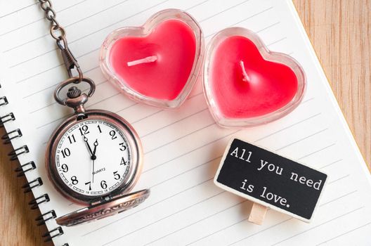 All you need is love. Red heart candle and pocket watch with open diary on wooden background.