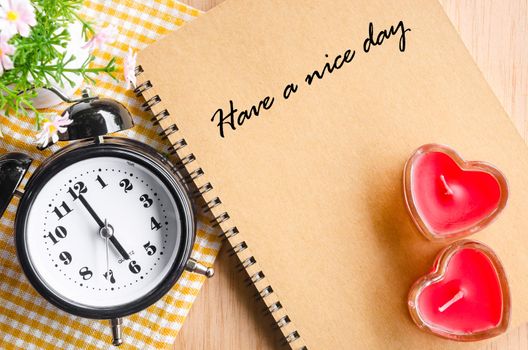 Have a nice day on brown diary and alarm clok with red heart on wooden background.