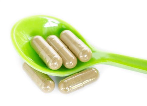 Herbal medicine capsules in green spoon on white background.