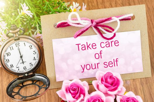 Take care of your self on tag and pocket watch with pink rose on wooden background.