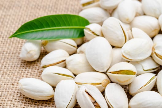 Pistachios and green leaf on sack background.