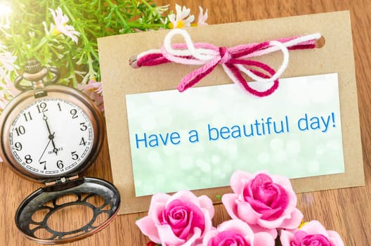 Have a beautiful day paper tag and pocket watch with pink rose on wooden background.
