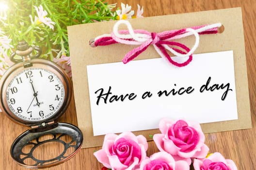 Have a nice day. Paper tag and pocket watch with pink rose on wooden background.