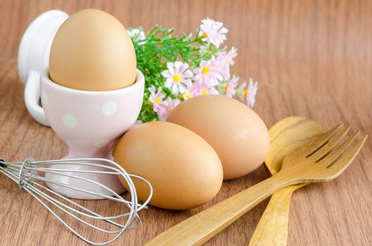Eggs and wooden spoon with flower on wooden background.