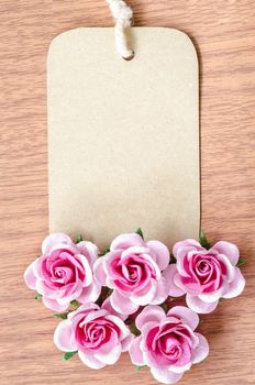 Brown paper tag and pink rose on wooden background for your text.