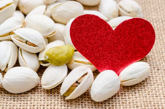 Pistachio nuts and Blank red paper heart tag on sack background.