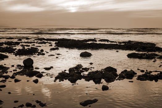 reflections at rocky beach near ballybunion on the wild atlantic way ireland with a beautiful sunset in sepia