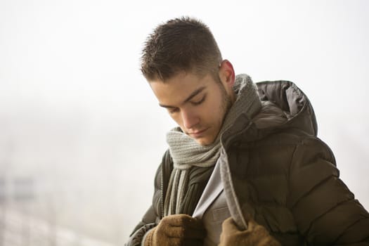 Profile view of handsome young man outdoor in winter wearing scarf, looking away thinking