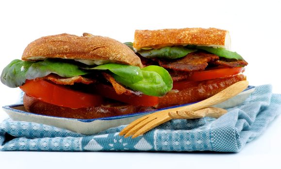 Ciabatta Sandwiches with Bacon, Tomato, Lettuce and Sauces on Plate with Napkin and Wooden Fork closeup on White background
