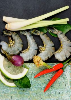 Ingredient of Thai Tom Yam Spicy Soup with Big King Shrimps, Lime, Lemon Grass, Chili Peppers, Ginger, Spices and Greens closeup on Slate and Wooden background