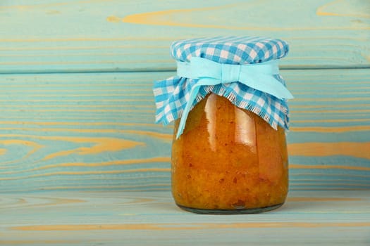 One glass jar of homemade quince jam with textile top decoration at blue painted vintage wooden surface