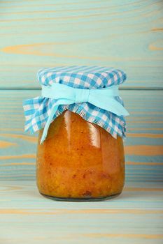 One glass jar of homemade quince jam with textile top decoration at blue painted vintage wooden surface