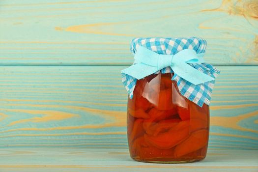 One glass jar of homemade quince jam with textile top decoration at blue painted vintage wooden surface